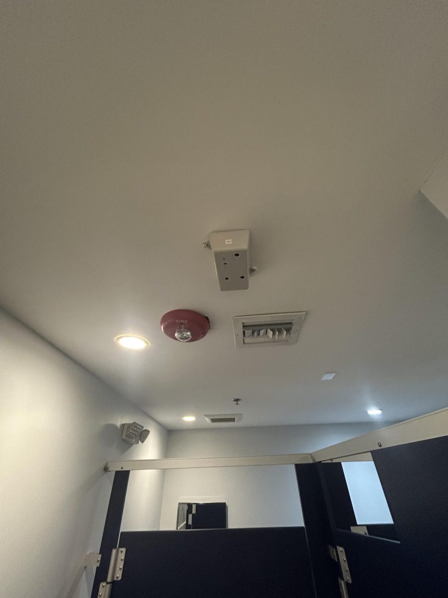 A vape detector, the large rectangular box, is shown fixated to the ceiling of the the library bathroom.